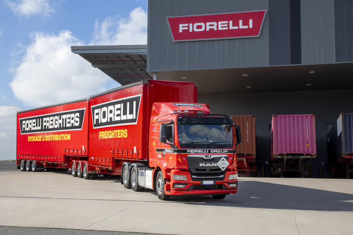 A long red truck with Fiorelli Freighters signage on the side is parked in front of a building with a Fiorelli sign on it.