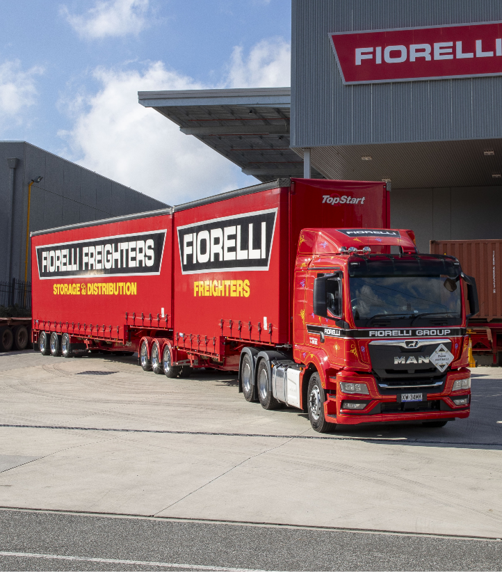 A long red truck with Fiorelli Freighters signage on the side is parked in front of a building with a Fiorelli sign on it.