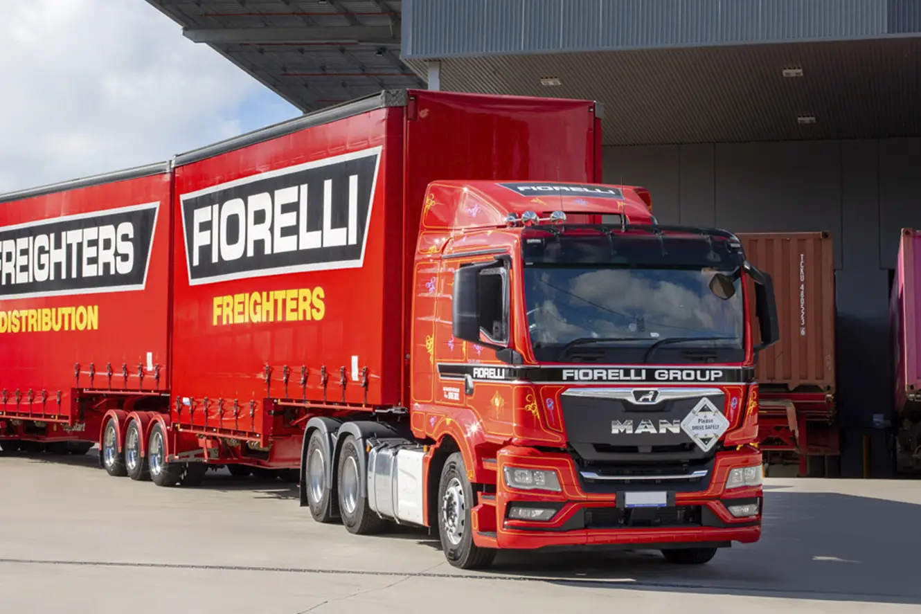 A long red truck with Fiorelli Freighters signage on the side is parked in front of a building with a Fiorelli sign on it.